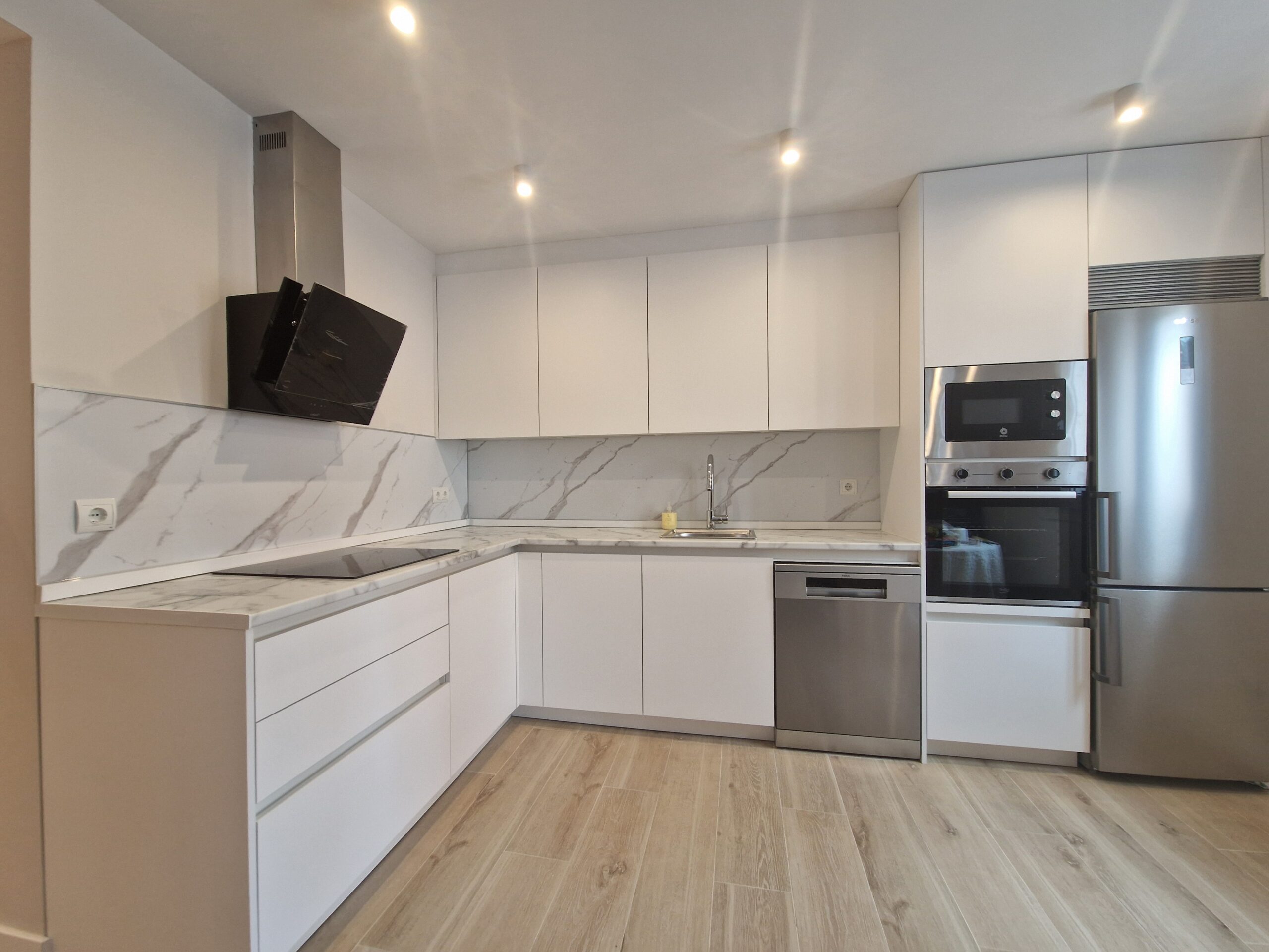 Cocina moderna blanca con encimera de mármol y electrodomésticos.