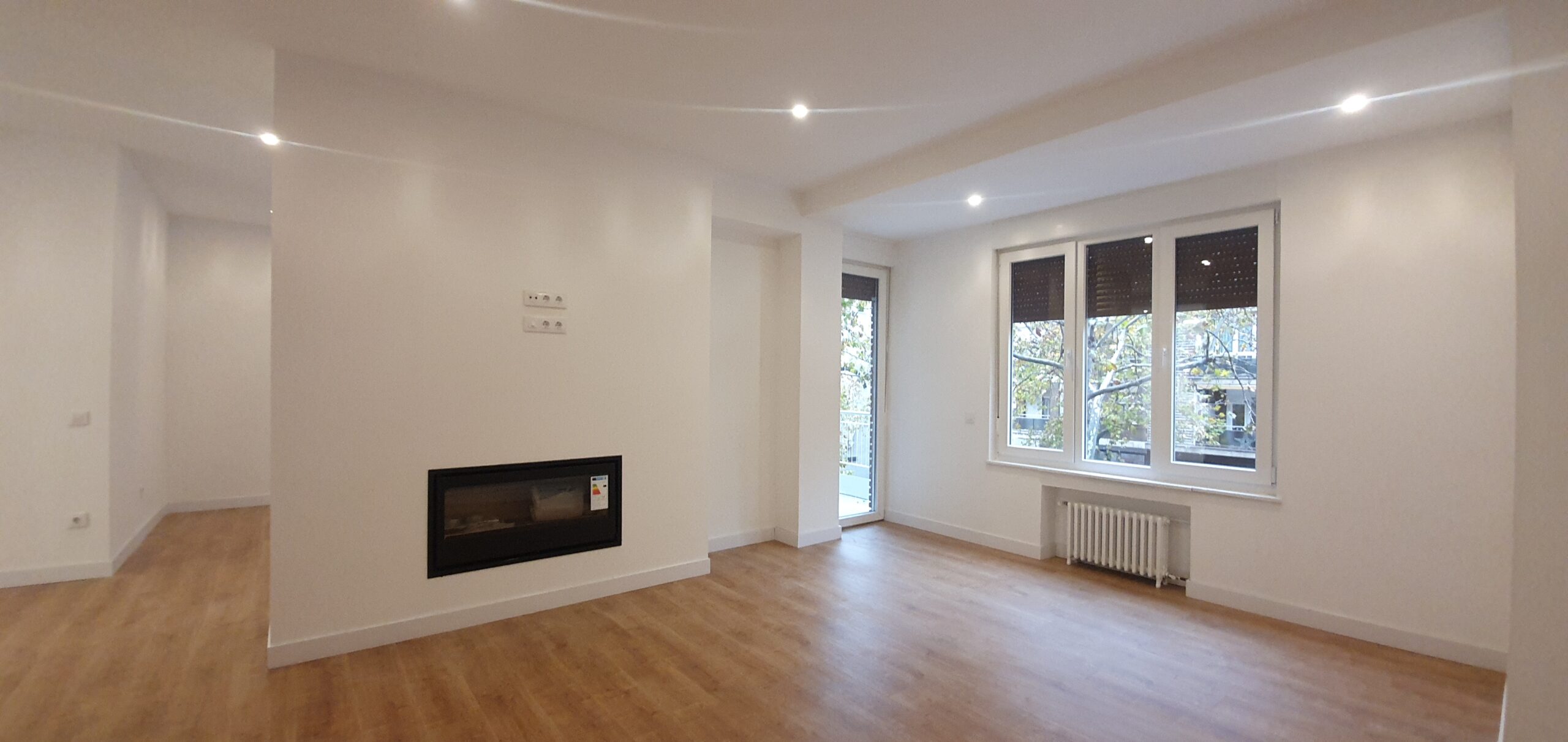 Salón vacío con chimenea y grandes ventanales blancos.