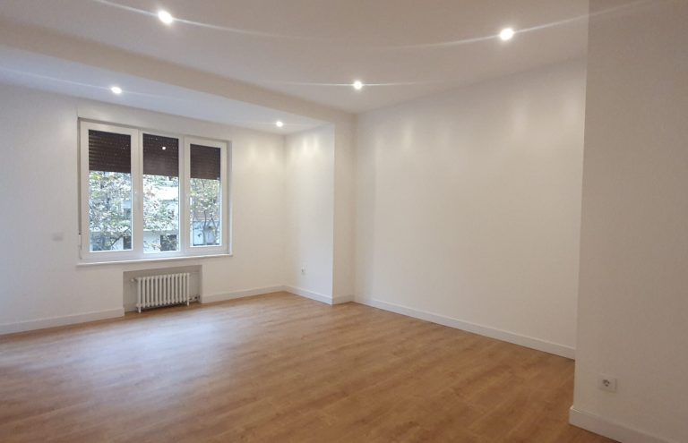 Salón vacío y luminoso con ventana y suelo de madera.