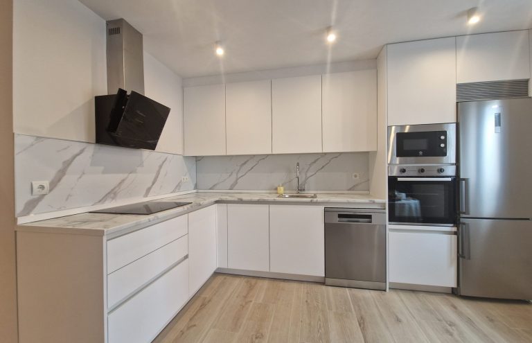 Cocina moderna blanca con encimera de mármol y electrodomésticos.