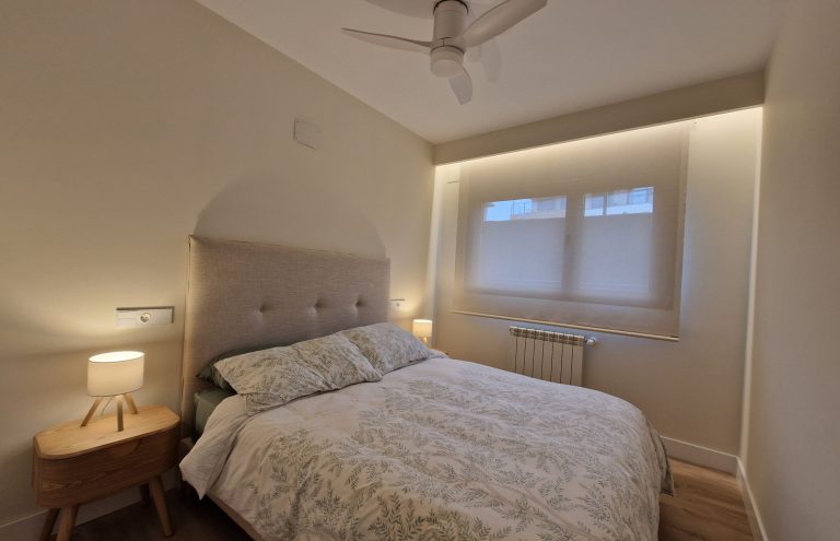 Dormitorio moderno con cama, mesita y ventilador de techo.