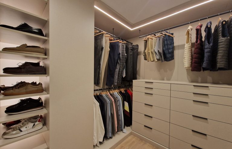Vestidor moderno con ropa, zapatos y cajones blancos.