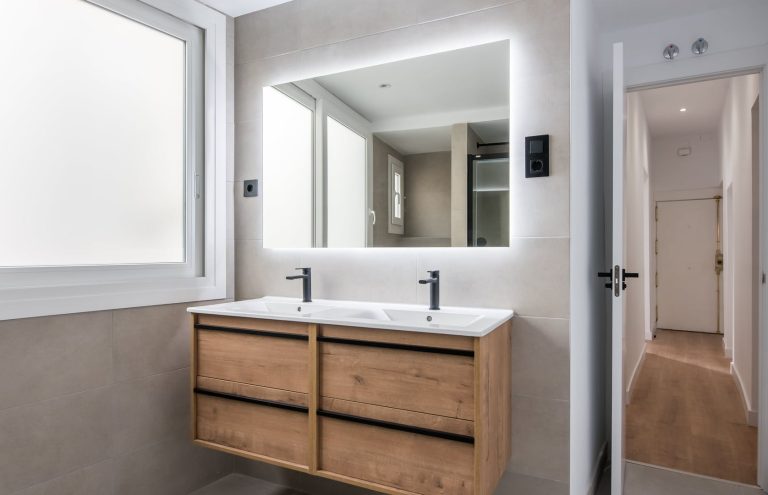 Baño moderno con lavabo doble y espejo iluminado.
